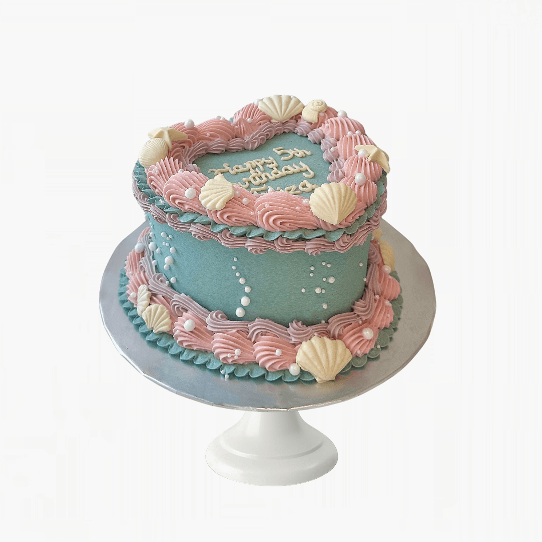 Two-tiered birthday cake with pink and blue frosting, shell decorations, and 'Happy Birthday' text on a white background - children's birthday cakes Sydney