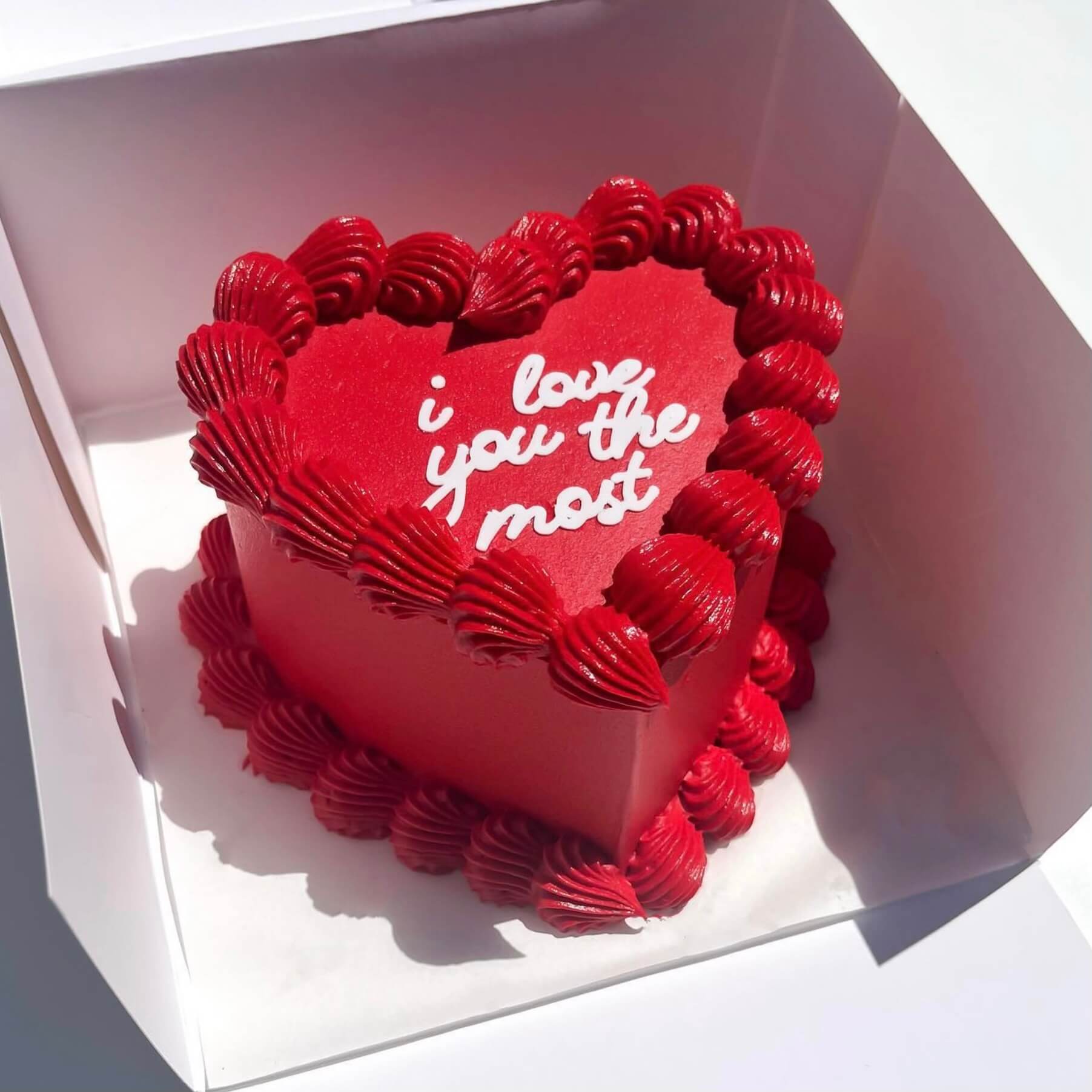 Red heart-shaped cake with 'I love you the most' text in a white box - Valentine's Day cake gift
