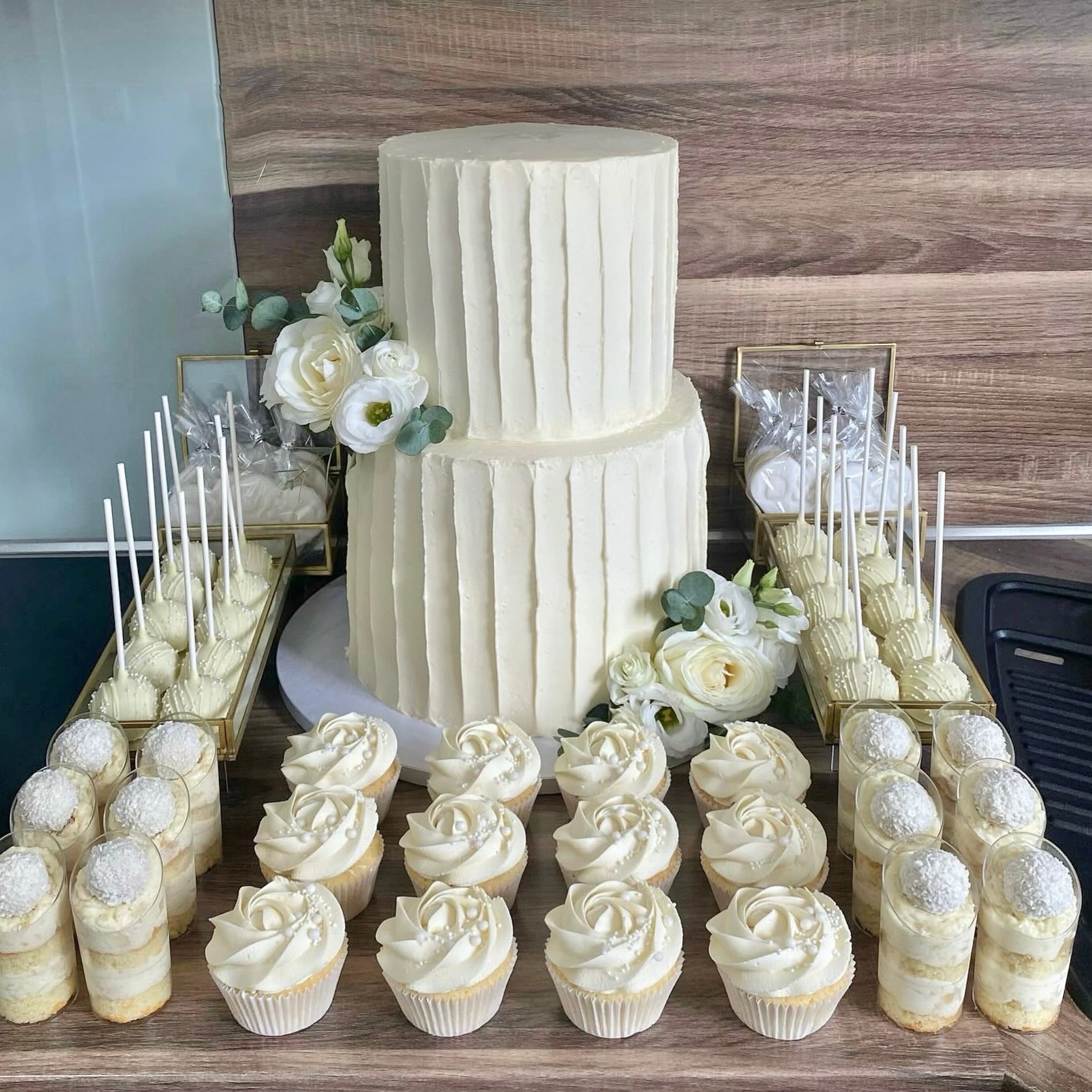 White wedding cake with cupcakes and cookies on a wooden table