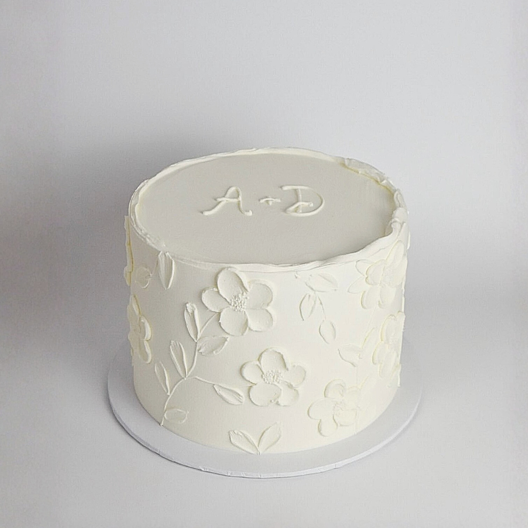 White cake with floral designs and initials on a grey background - gender reveal cakes Sydney