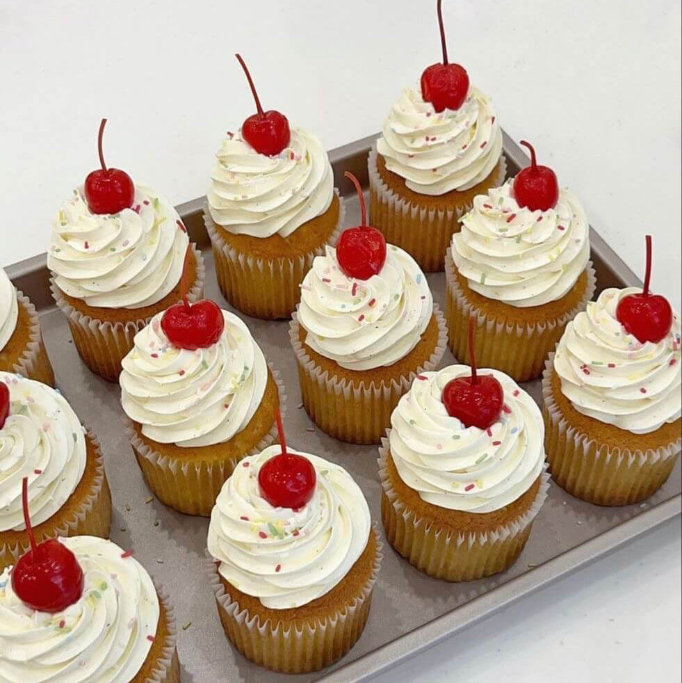 Cupcakes with white frosting and red cherries on a tray