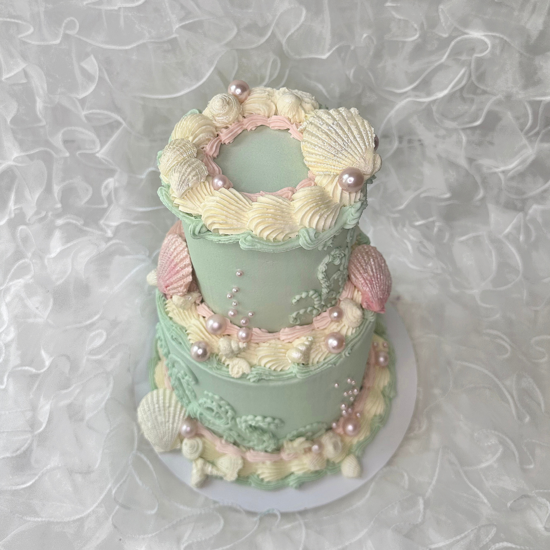Pastel-colored cake with shell and pearl decorations on a textured white background - custom cakes Sydney