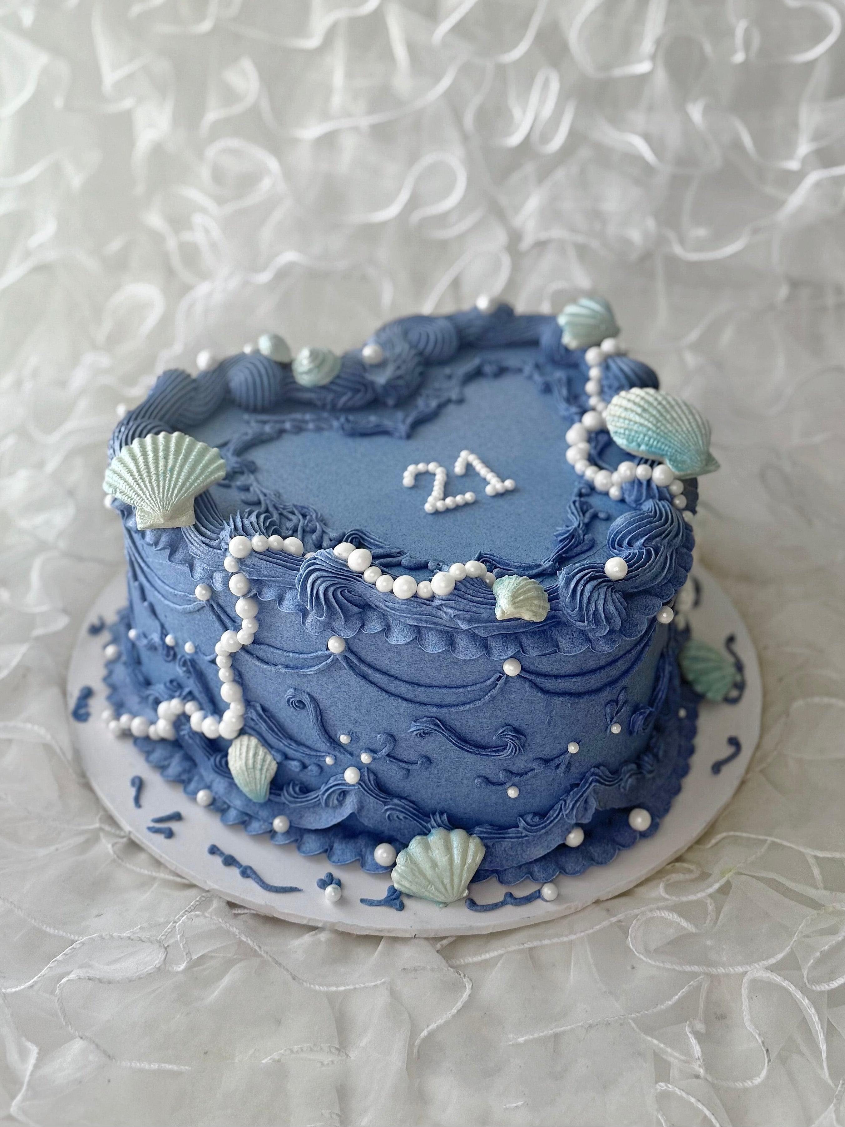 Blue cake with decorative seashells and pearls on a textured blue background