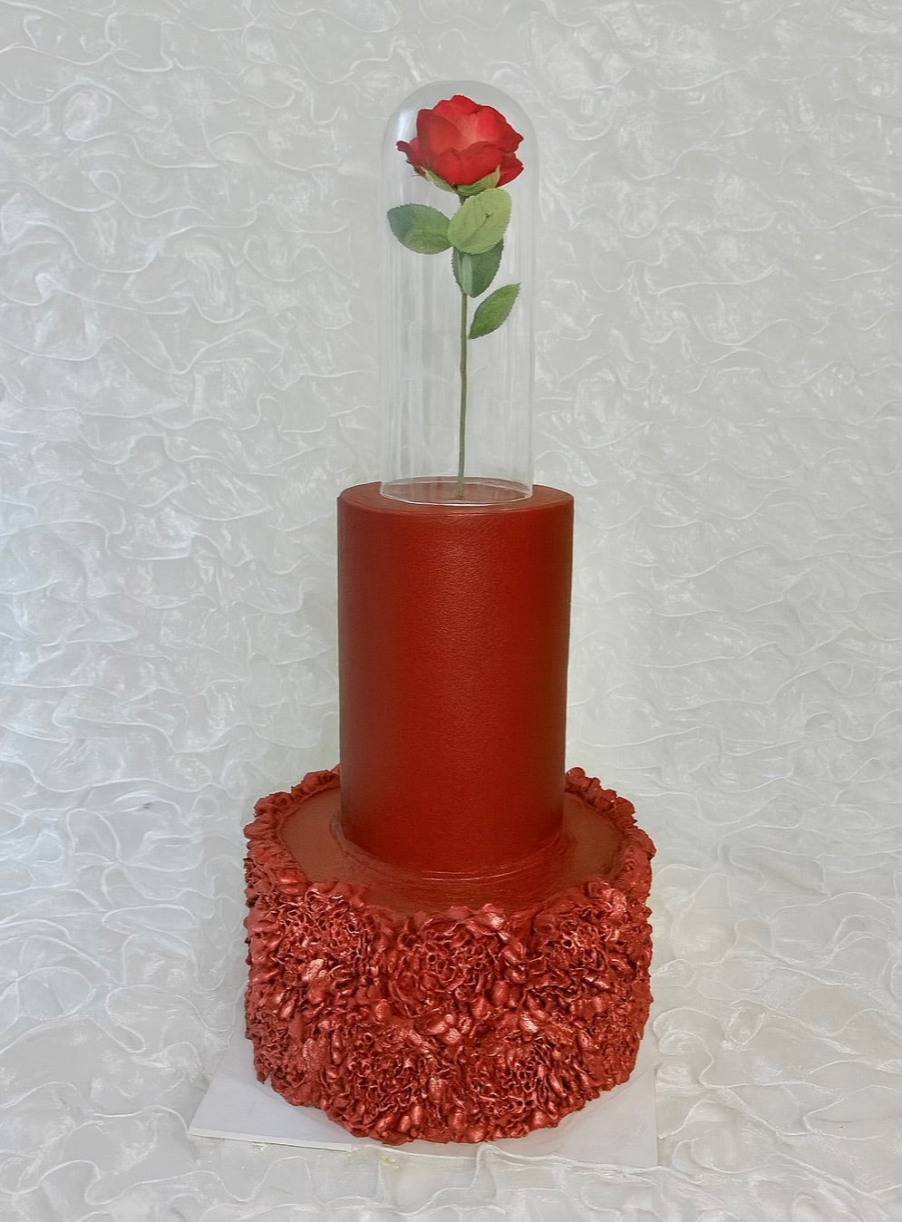 A three tiered red cake with a red rose in a glass dome and a textured red base 