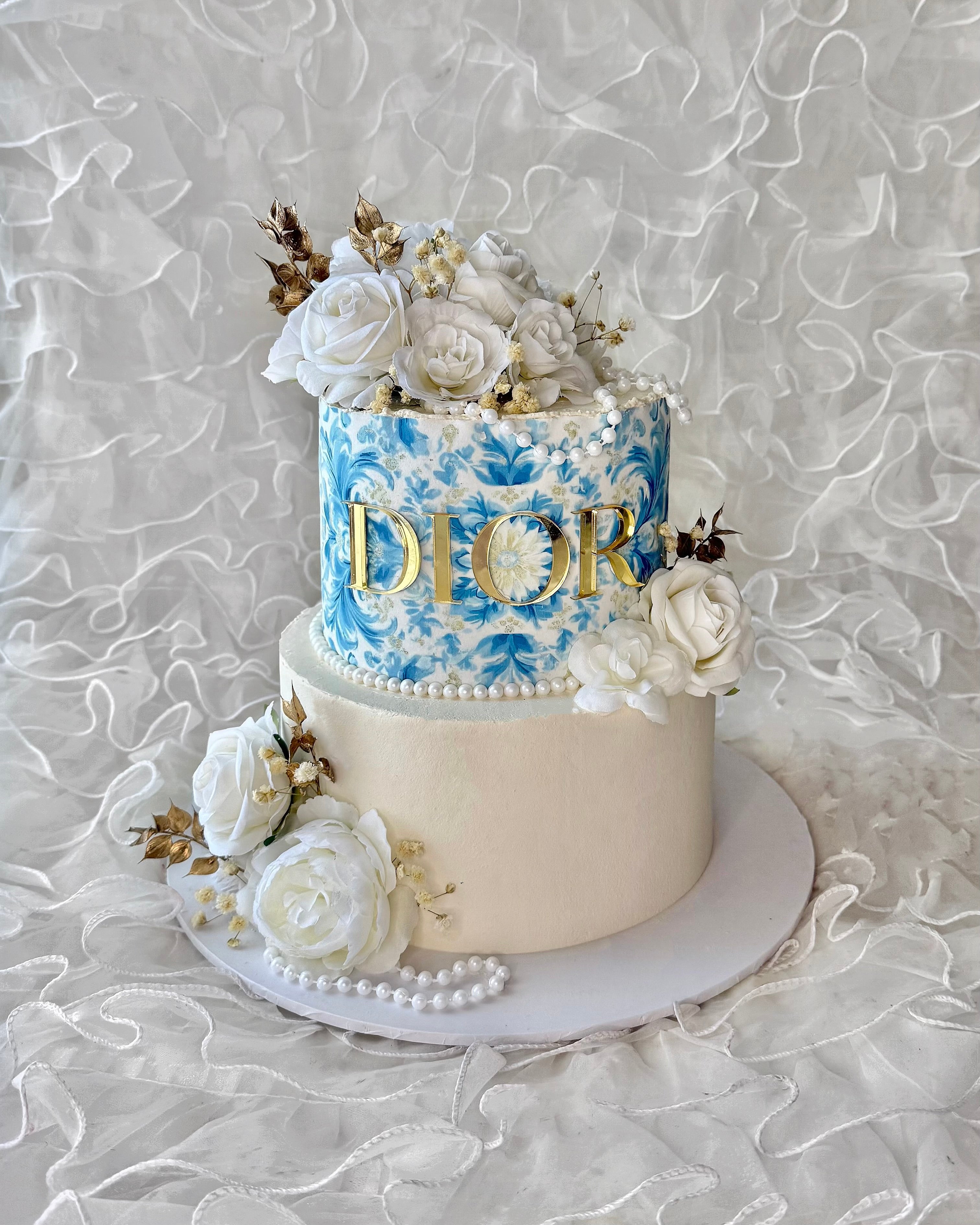 Two-tiered cake with floral decorations and 'Dior' branding with blue floral detailing.