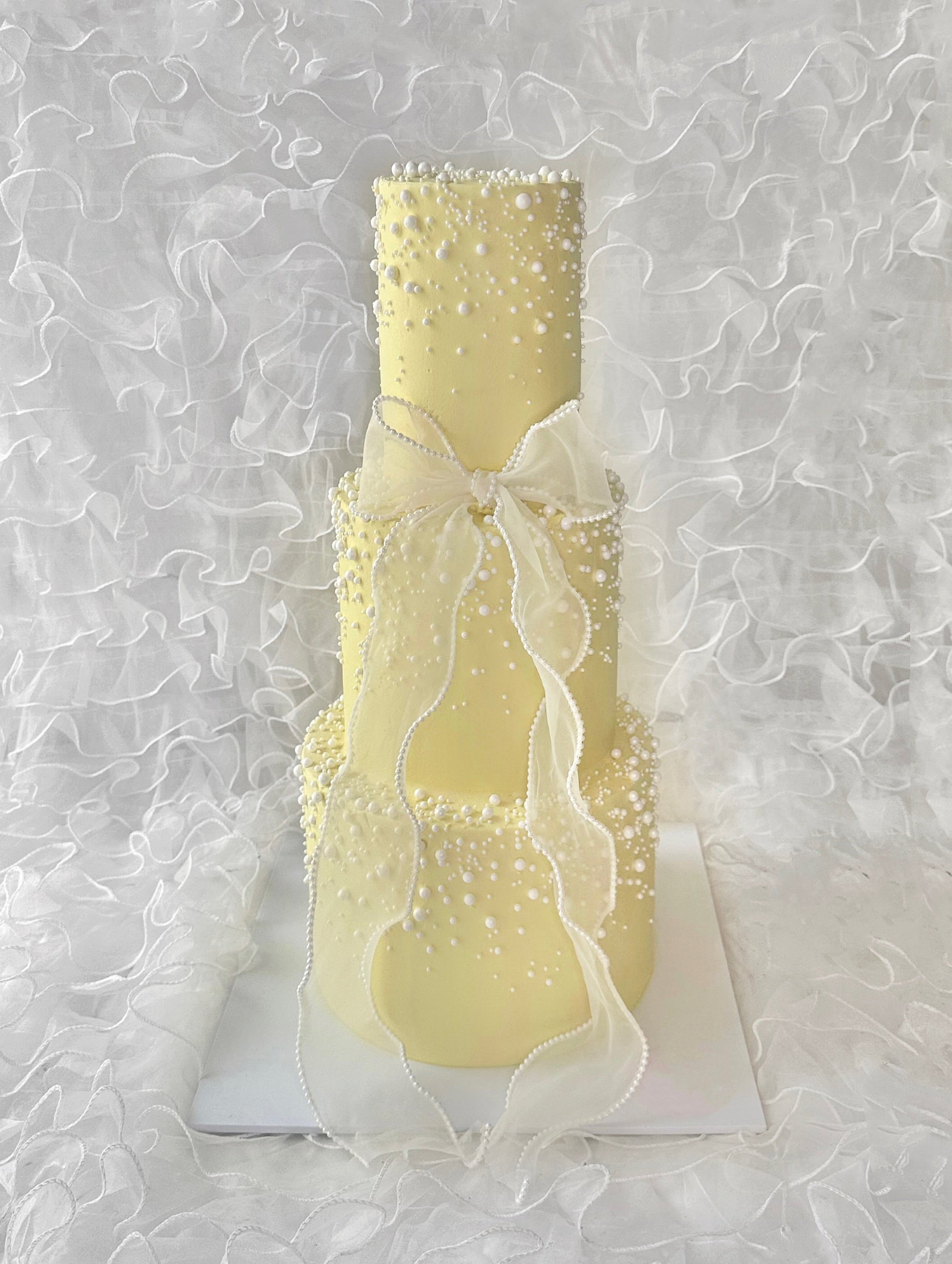 A three tiered yellow cake with pearl and bow detailing 