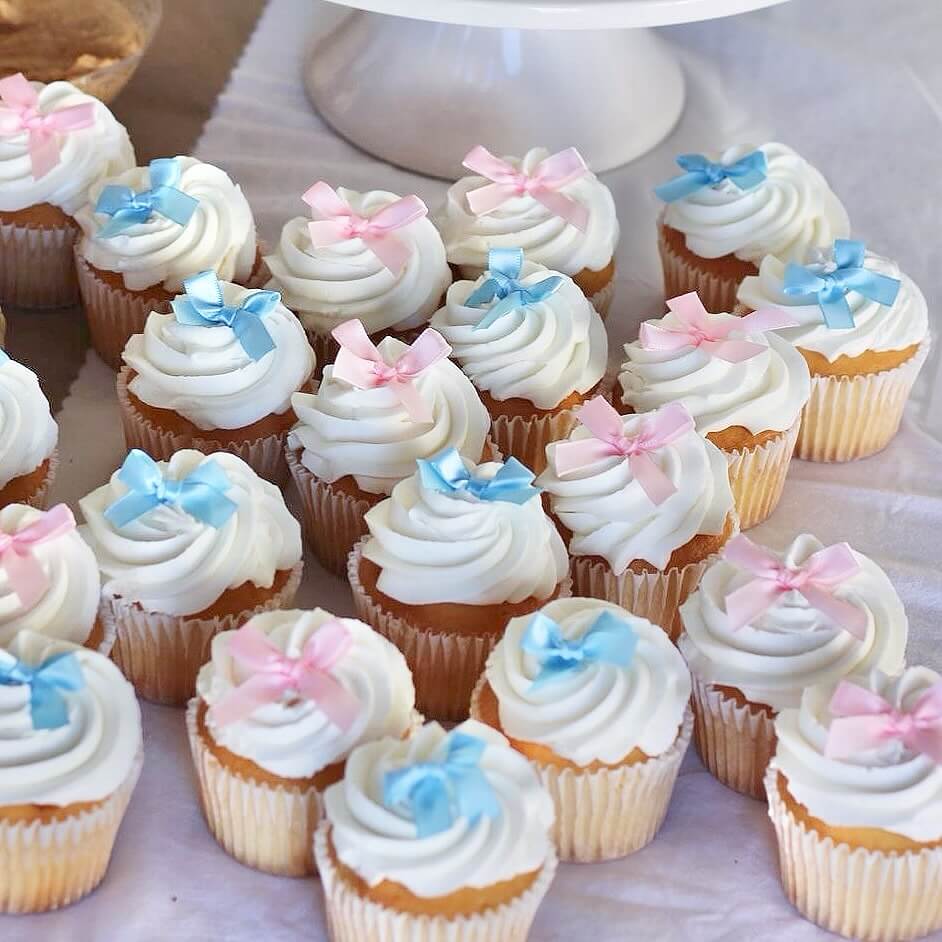 Gender reveal Cupcakes with white frosting and colorful bows on a white surface
