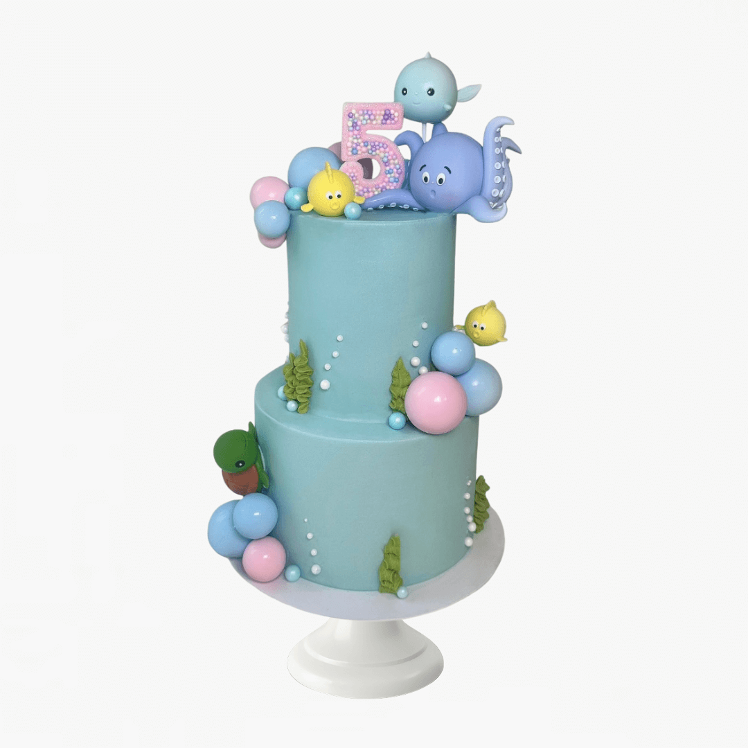 Two-tiered blue cake with ocean-themed decorations on a white stand - children's birthday cakes 