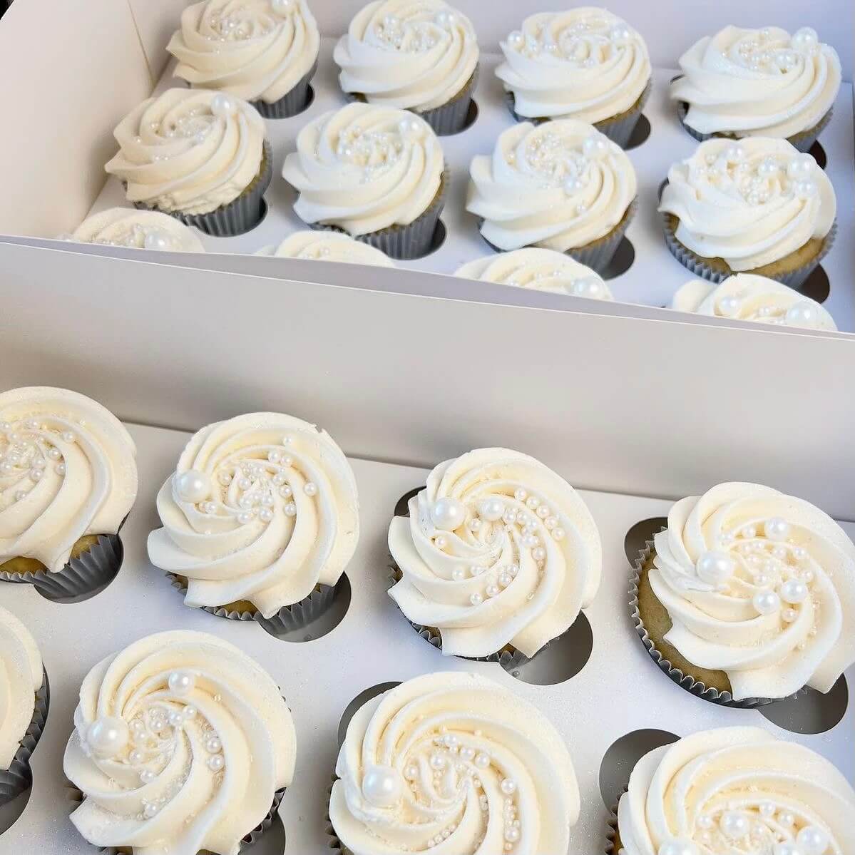 Box of cupcakes with white frosting and decorative elements