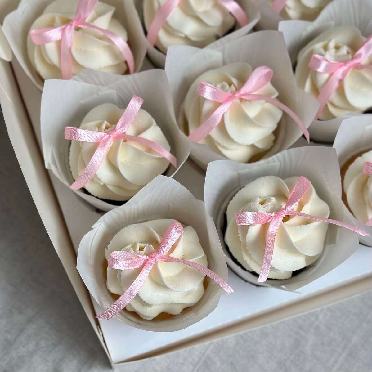 Cupcakes with white frosting and pink ribbons in a box