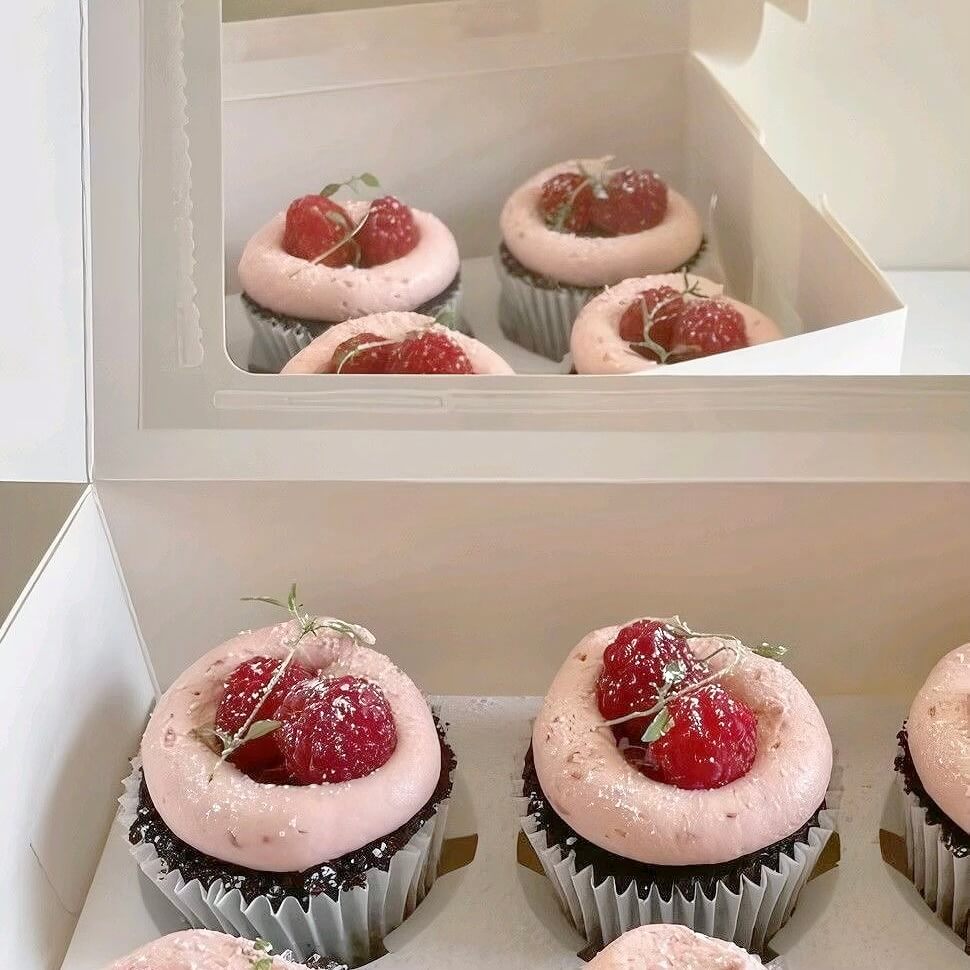 Cupcakes with pink frosting and raspberries in a white box
