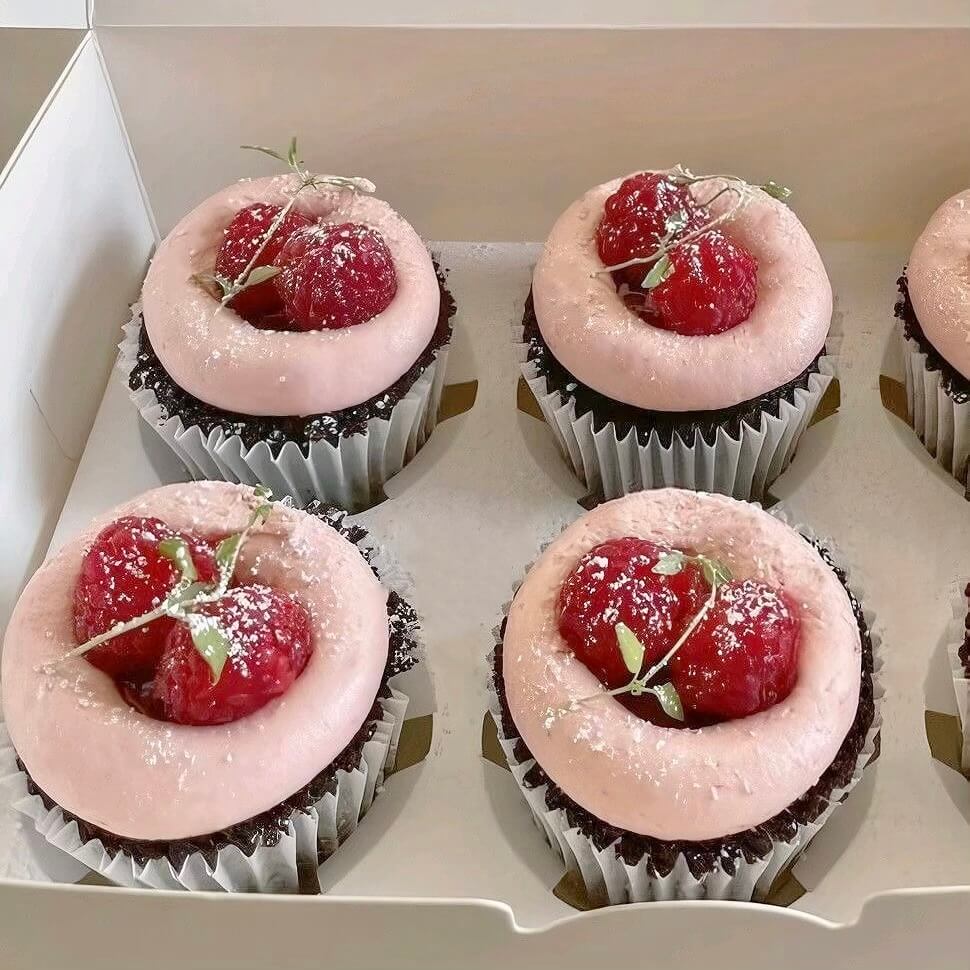 Cupcakes with pink frosting and raspberries in a box