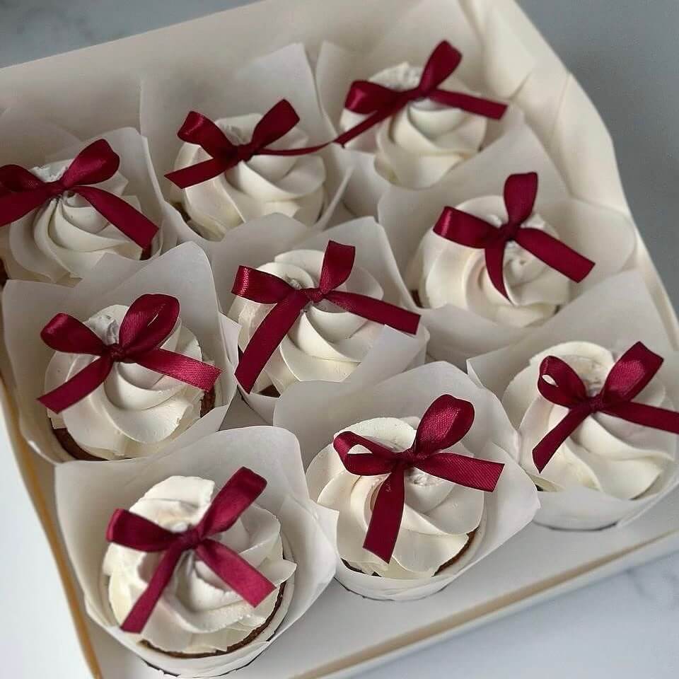 Cupcakes with white frosting and red ribbons arranged in a box.