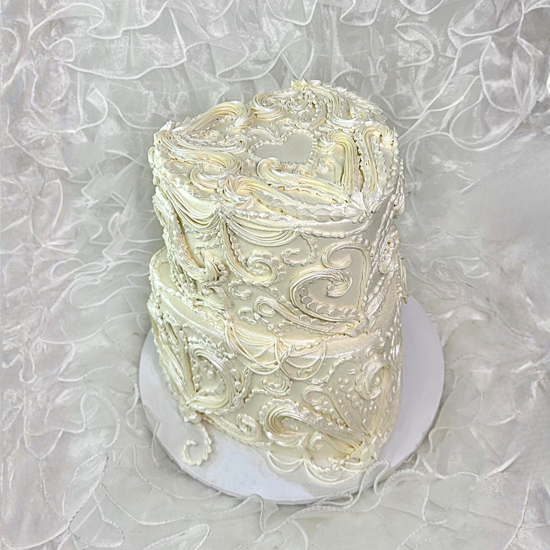 Two-tiered cake with intricate white frosting design on a textured gray background